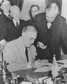 President Roosevelt signs Declaration of War while surrounded by four congressmen.
