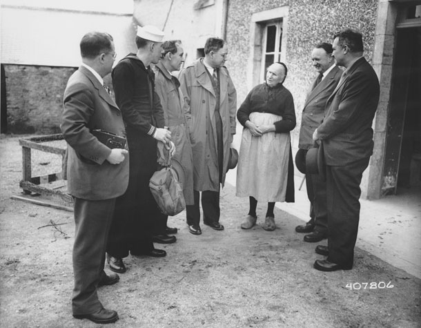 Photo of senators talking to old woman outside her house.
