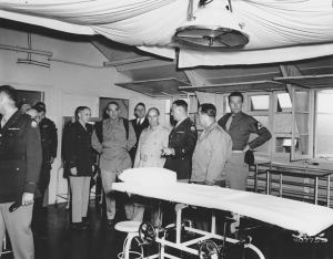 Photo of a group of senators and military men inspect hospital operating room.