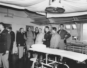 Photo of a group of senators and military men inspect hospital operating room.