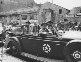 Photo of four senators riding in open-topped car.