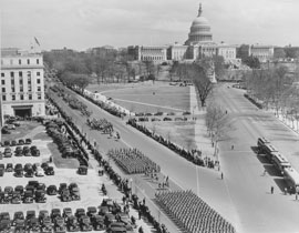 Photo of a military parade on a street next to the Capitol Building.