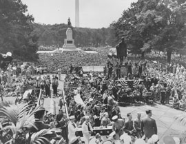 Photo of a large crowd of people gathered with Washington Memorial in background. 